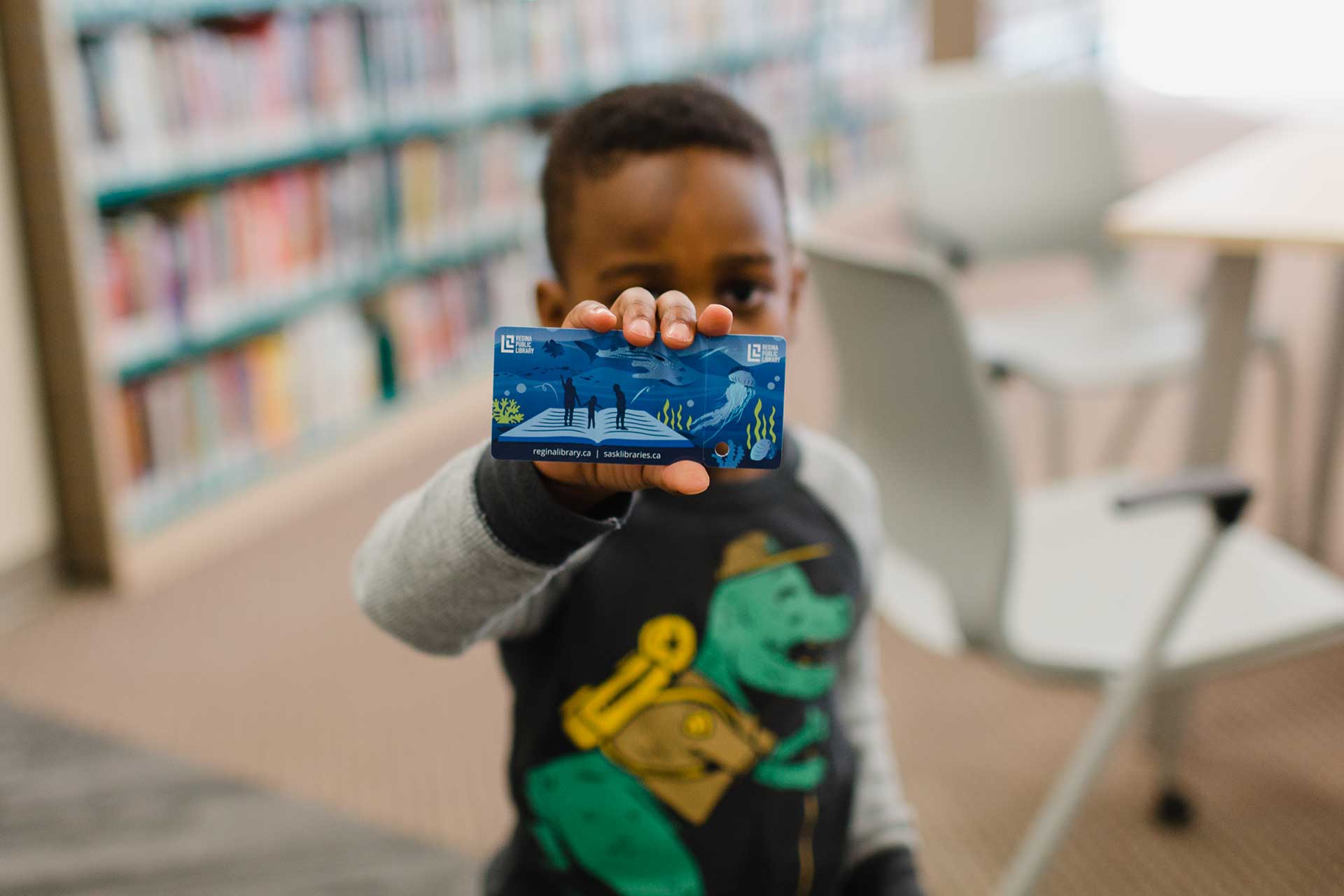 Inside the Regina Public Library, a young child holds up a new library card.