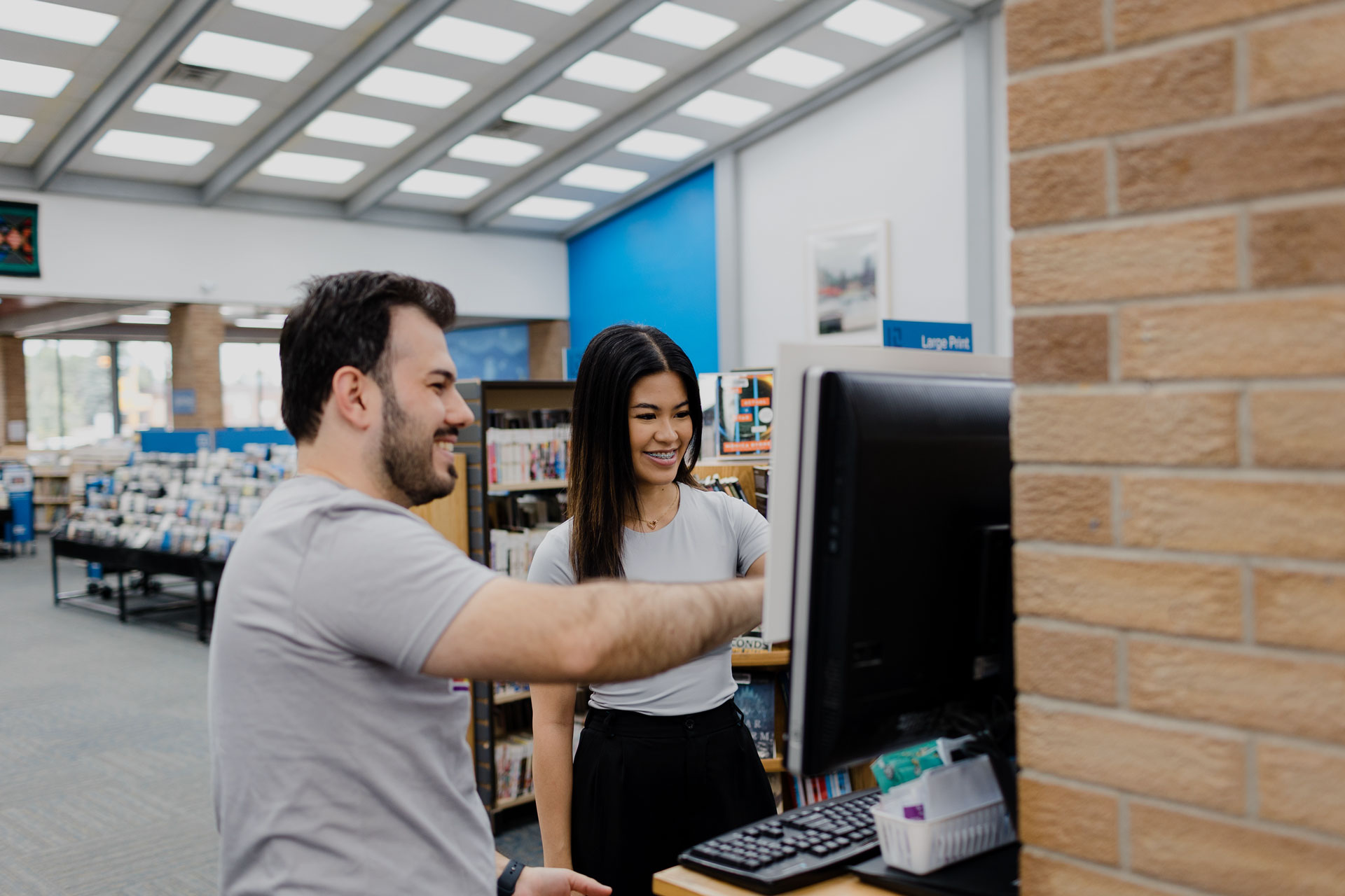 Friendly library employee helps young woman at a computer kiosk in the Regina Public Library